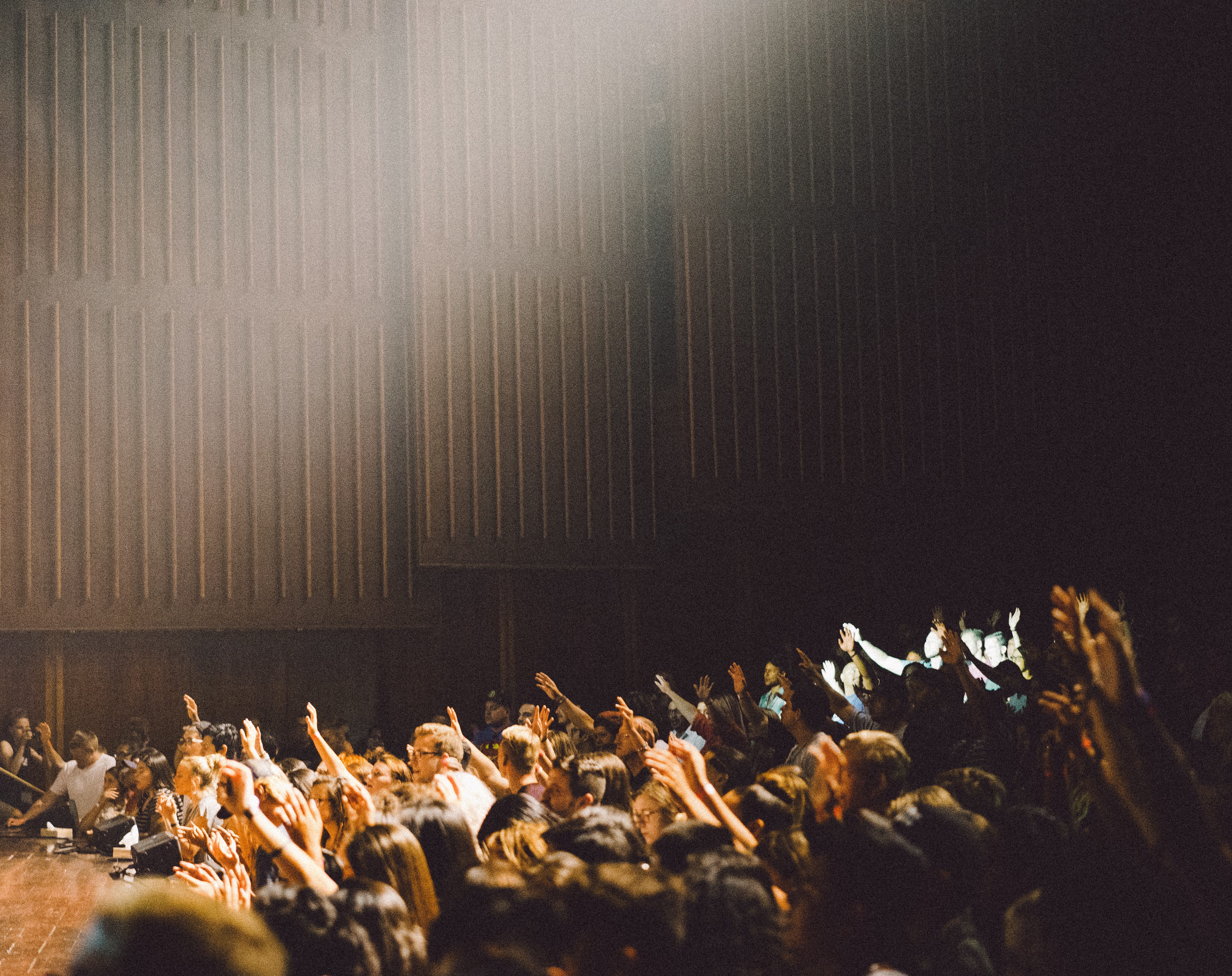 photo of a crowd in an auditorium with many people raising their hands